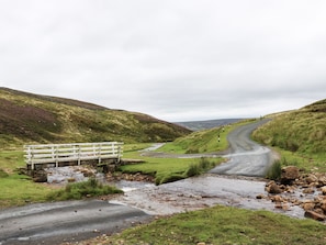 Un camino rural con una cerca blanca y un puente de piedra sobre un arroyo.