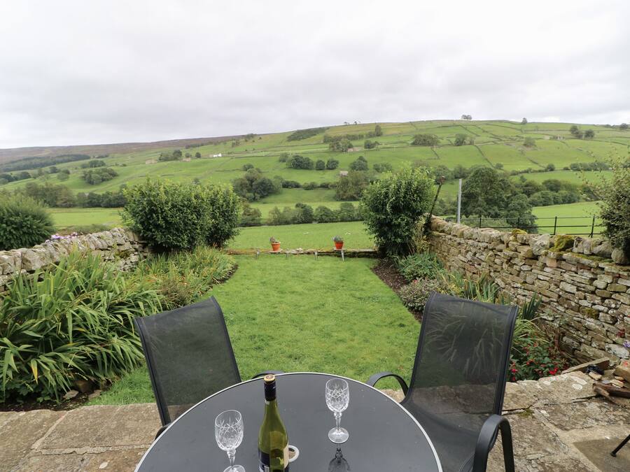 A table with a bottle of wine and two glasses, set against a scenic hillside view.