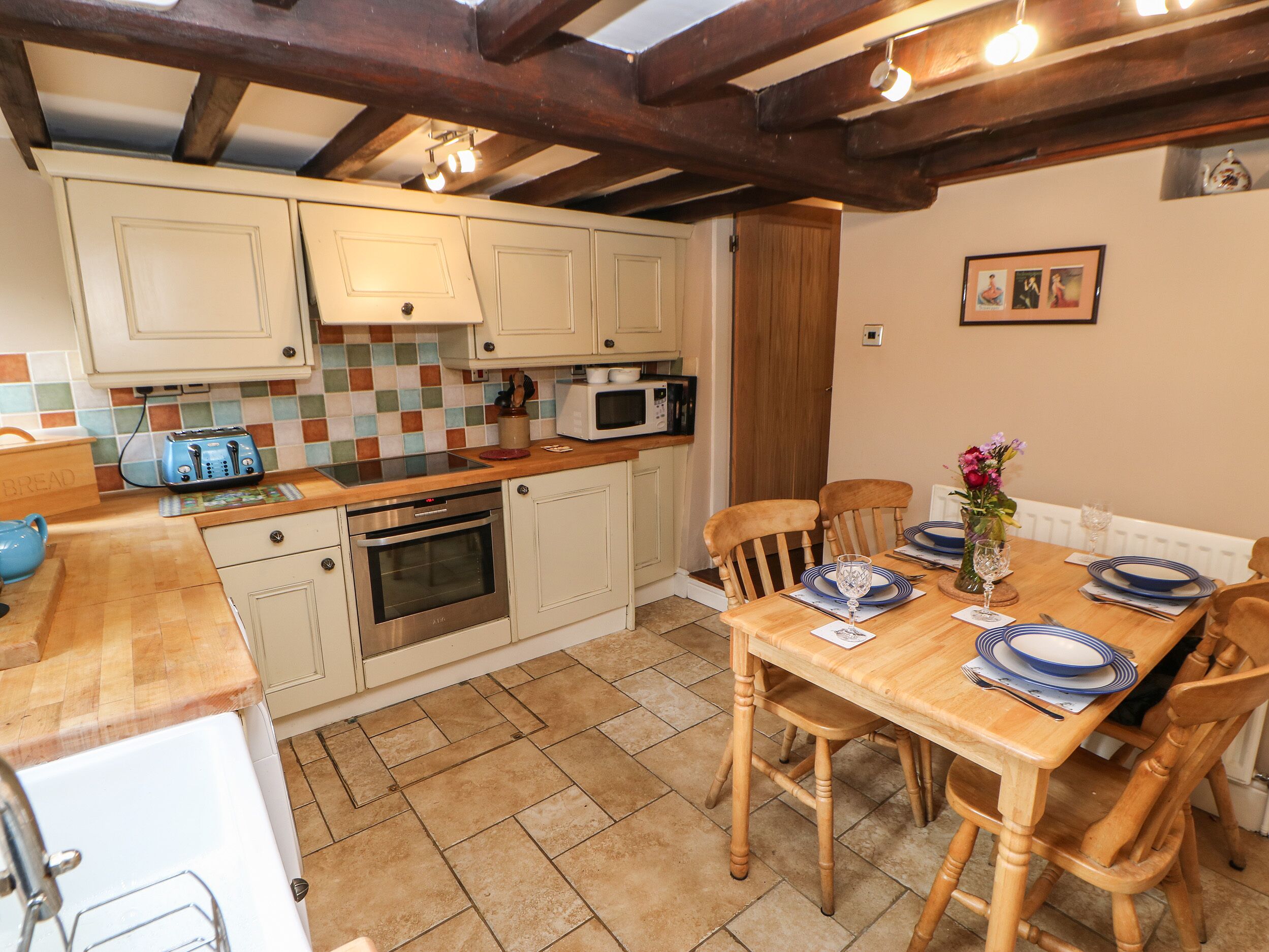 A kitchen with white cabinets, a wooden countertop, a built-in oven, and a dining table set with plates and glasses.