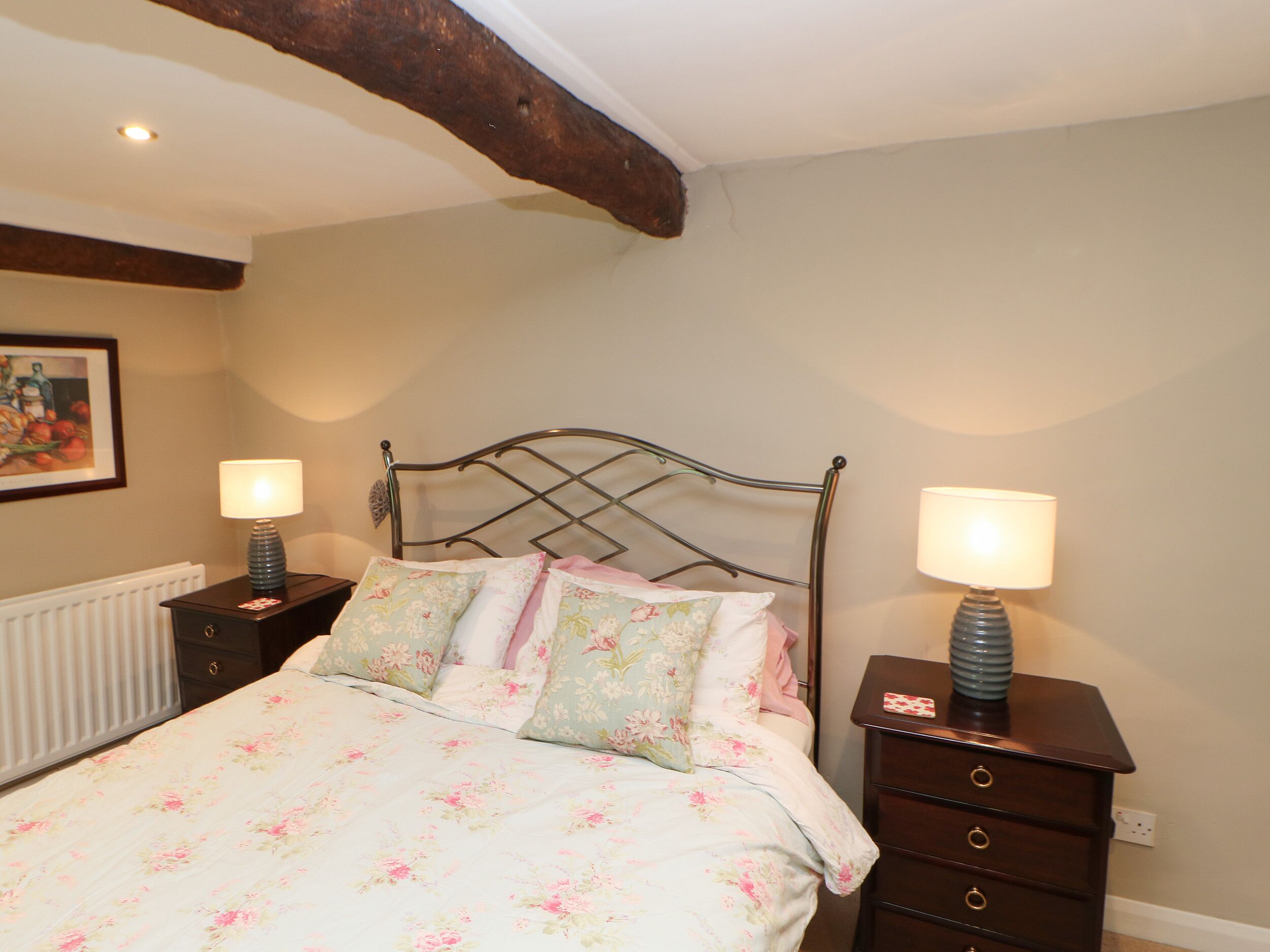 A bedroom with a bed, two bedside tables, a dresser, and a painting on the wall.