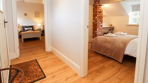 A bedroom with a wooden floor, a brick accent wall, a bed with a beige blanket, and a desk with a chair. - Commonwood Cottage (Wrexham)
