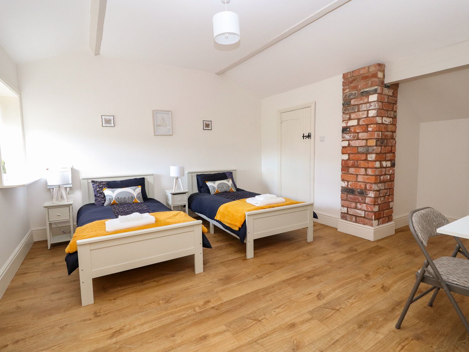 A room with two beds, a brick wall, a white door, and a desk with a chair.