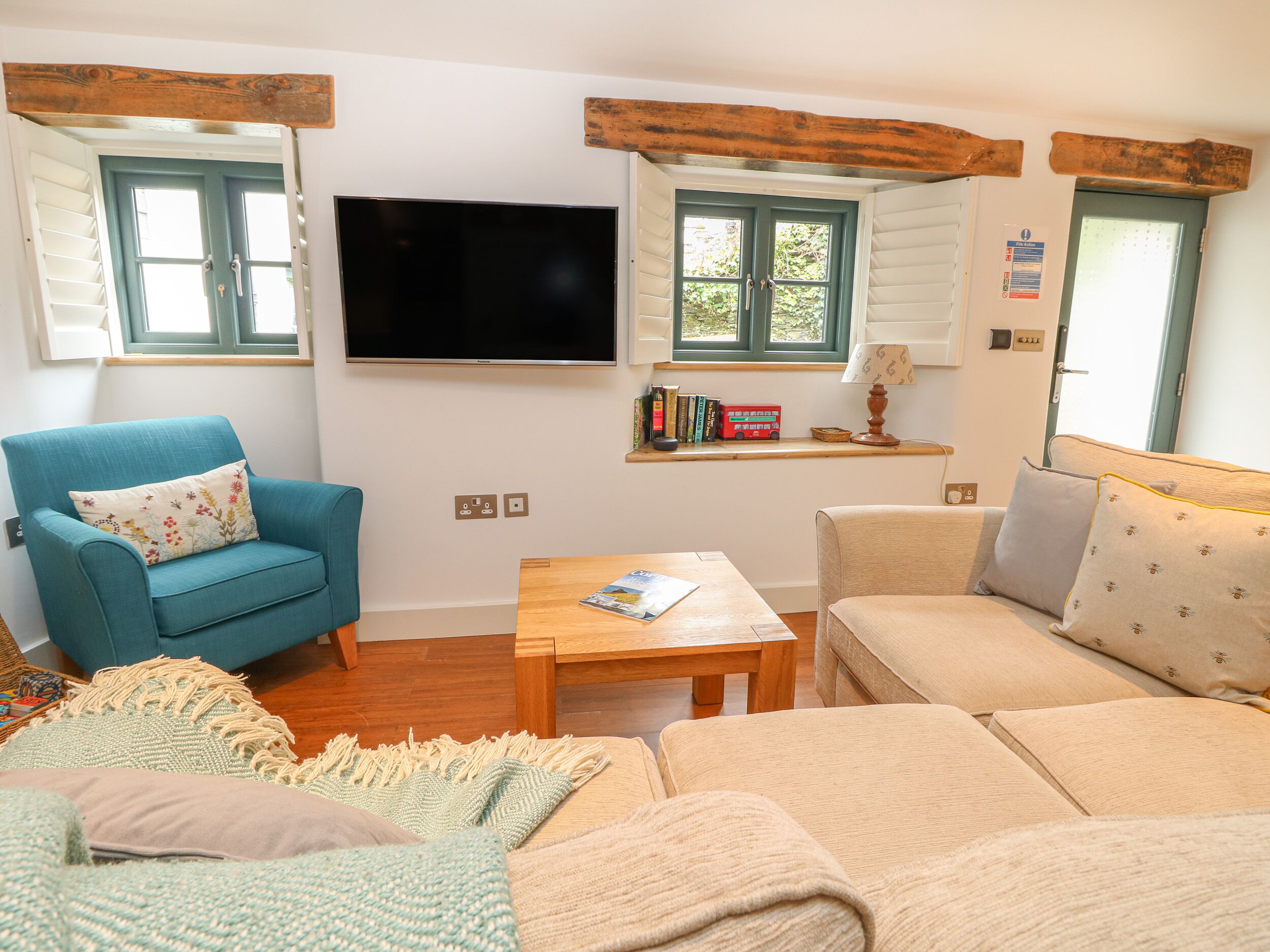 Una sala de estar acogedora con un sillón azul, un sofá beige, una mesa de centro de madera y un televisor de pantalla plana montado en la pared.