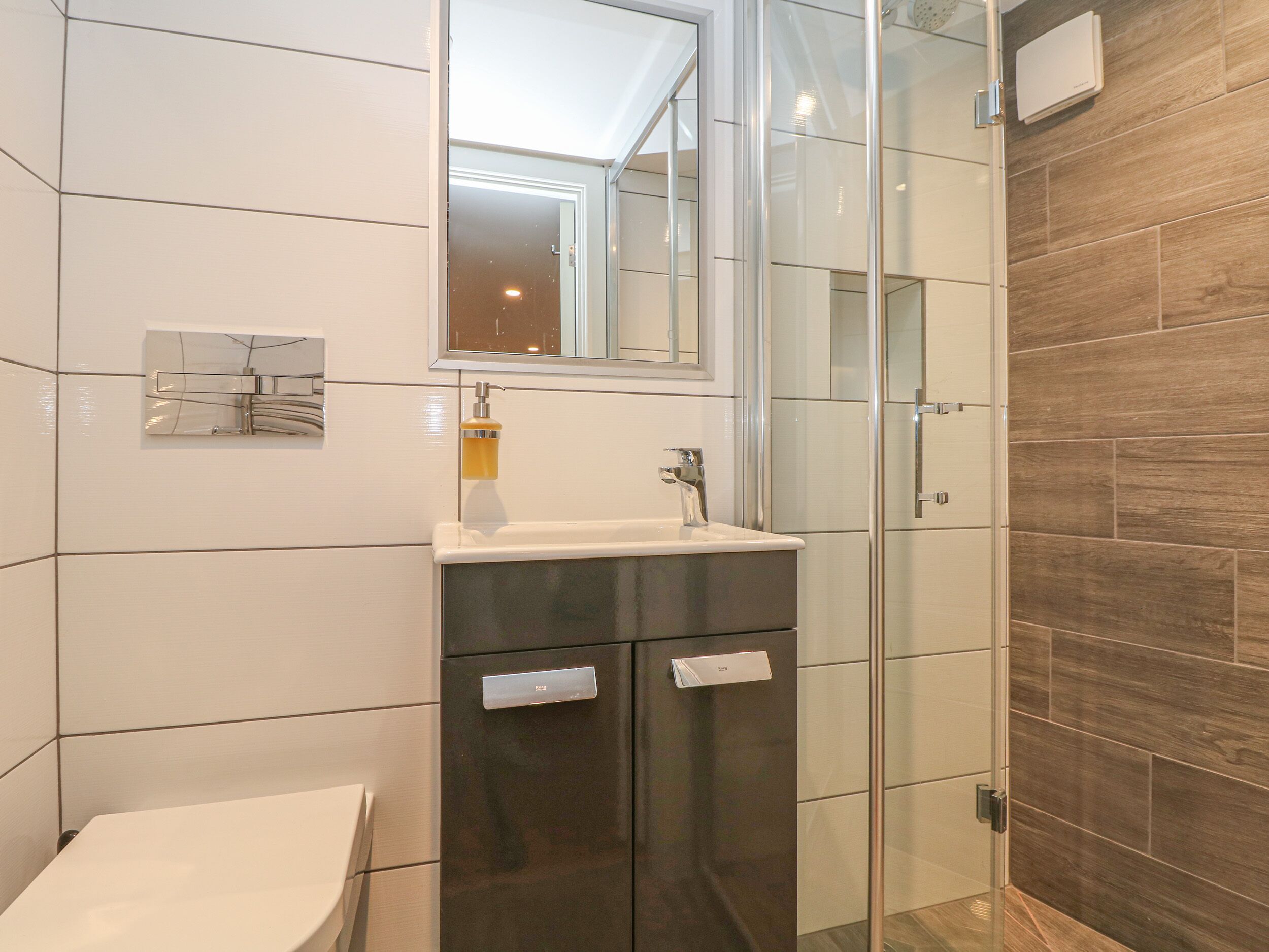 A modern bathroom with a glass shower enclosure, a white sink, and a dark vanity.