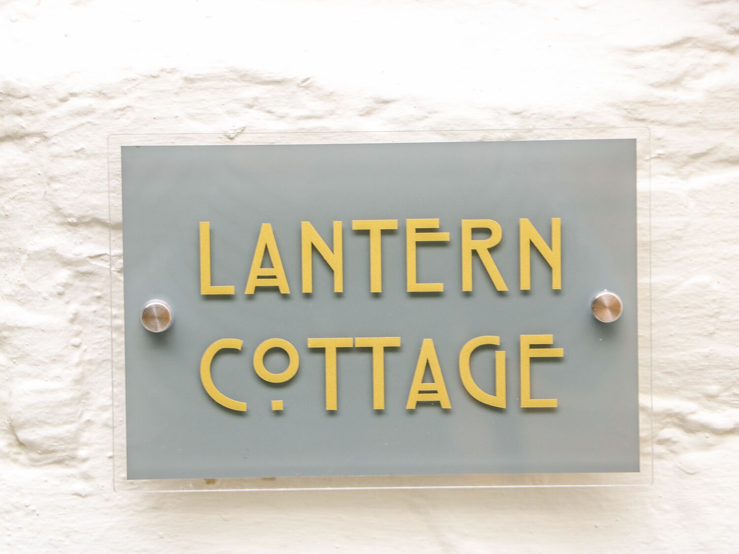 A sign with the text "LANTERN COTTAGE" mounted on a textured wall.