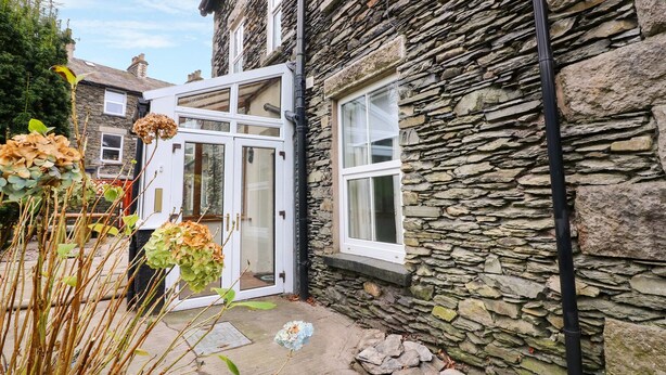 A stone building with a white door and windows, a stone pathway, and some plants. - Giddy Goose (Windermere)