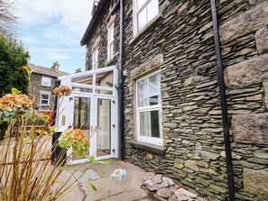 A stone building with a white door and windows, surrounded by plants and a stone pathway. - Giddy Goose (Windermere)