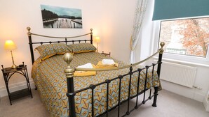 A bedroom with a bed, a nightstand, a lamp, a window with a view, and a painting on the wall. - Giddy Goose (Windermere)