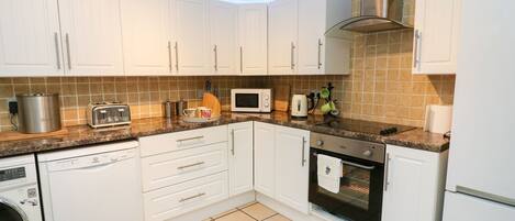 A modern kitchen with white cabinets, a microwave, a toaster, a kettle, and a dishwasher.