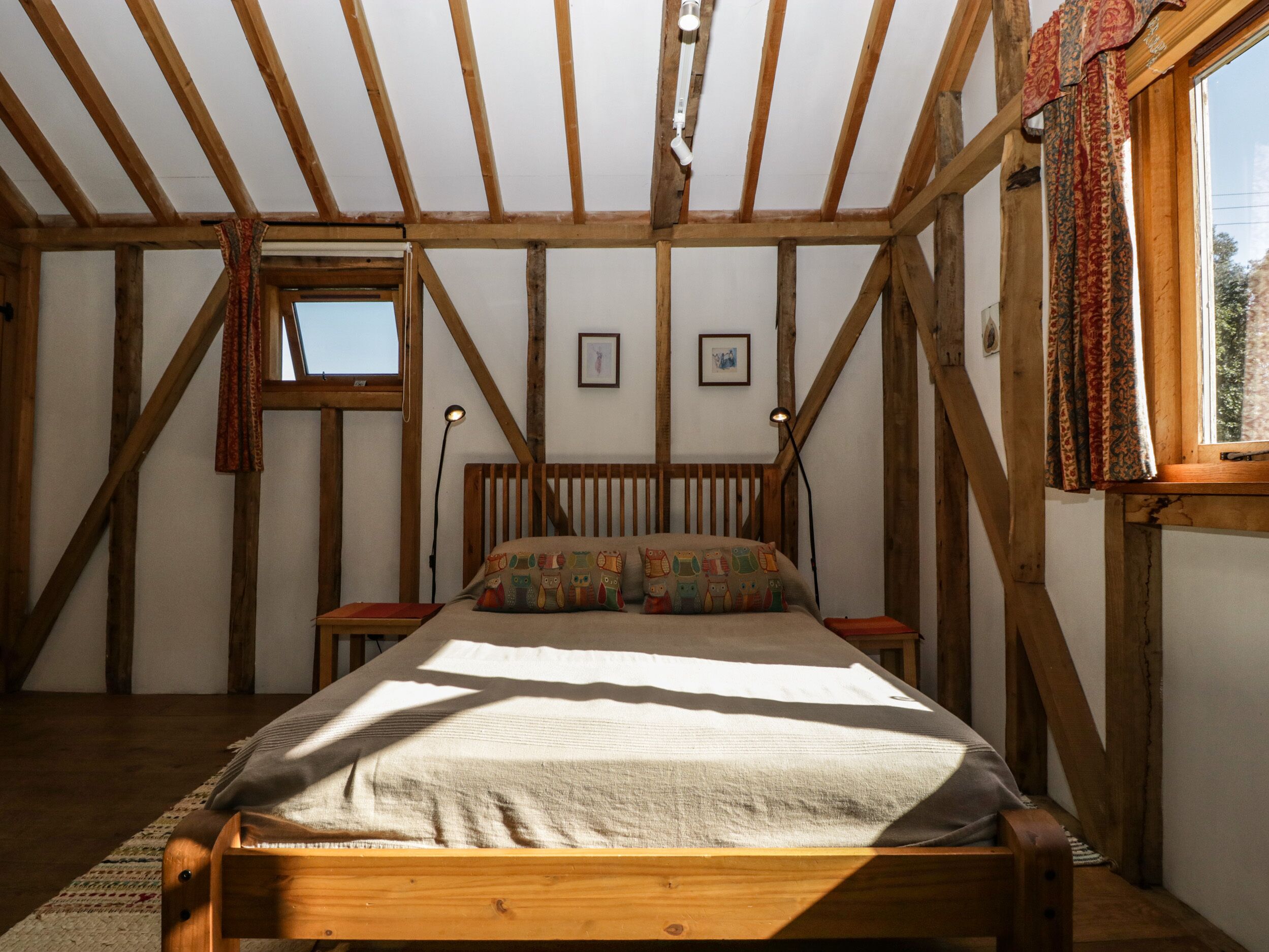 A bedroom with a wooden ceiling, a bed with a patterned pillow, two bedside tables, and a window with curtains.