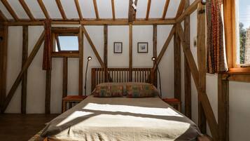 A bedroom with a wooden ceiling, a bed with a patterned pillow, two bedside tables, and a window with curtains.