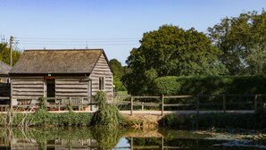 A rustic wooden cabin with a porch, surrounded by a wooden fence and lush greenery. - The Little Granary (Fordingbridge)