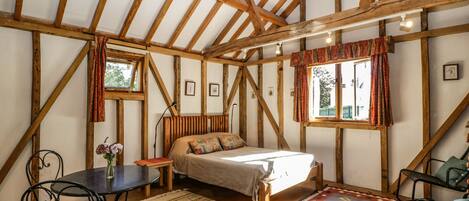 A cozy bedroom with a wooden ceiling, a bed, a small table, and a chair.