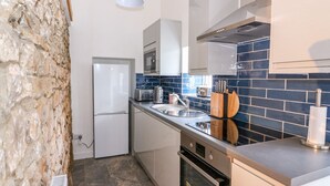 A compact kitchen with a stone wall, a refrigerator, a microwave, a toaster, a sink, and a stove. - Crooked Hill Cottage (Ammanford)