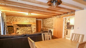 A cozy room with a stone fireplace, a wooden ceiling, a leather sofa, and a wooden dining table with chairs. - Crooked Hill Cottage (Ammanford)
