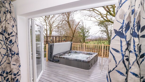 A hot tub on a wooden deck with a glass door leading to a garden. - Crooked Hill Cottage (Ammanford)