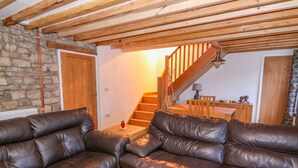 A cozy living room with leather sofas, a wooden staircase, and a stone wall. - Crooked Hill Cottage (Ammanford)