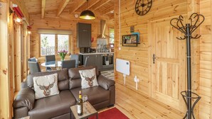 A cozy cabin interior with a wooden ceiling, a dining area, a sofa with deer-themed cushions, and a coat rack. - Sunnyside Lodge (Crewkerne)