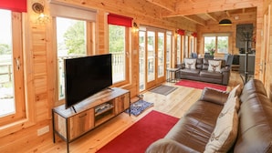 A wooden cabin interior with a TV, sofa, and dining area. - Sunnyside Lodge (Crewkerne)
