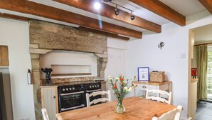 A kitchen with a stone wall, wooden beams, a stove, and a dining table with chairs. - Silver Hill Cottage (Harrogate)