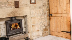 A stone fireplace with a wood-burning stove, a wooden door, and a framed picture on the wall. - Silver Hill Cottage (Harrogate)