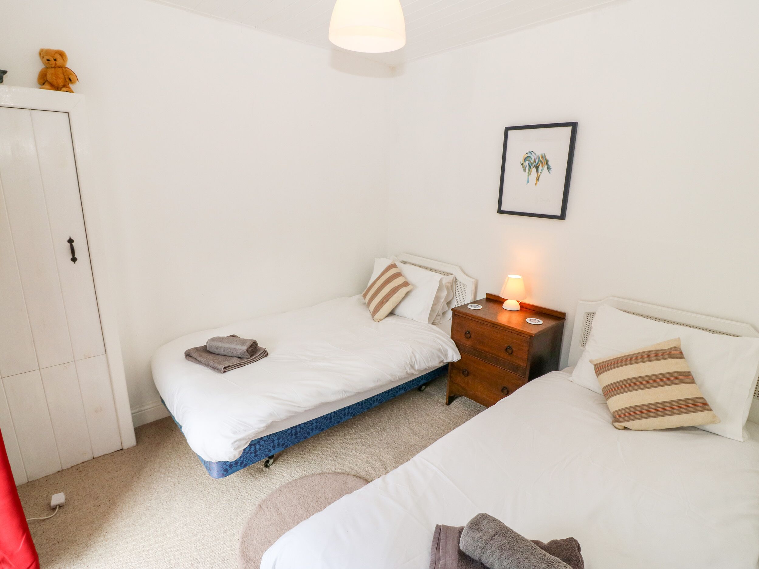 A bedroom with two beds, a wardrobe, a bedside table with a lamp, and a framed picture on the wall.
