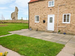 Traditional two-story house with a white front door and a small porch area, set amidst a grassy landscape with a historic stone structure in the background.