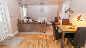 Un salon chaleureux avec un canapé marron, une table à manger avec des chaises, un ventilateur de plafond et un élément décoratif mural.
