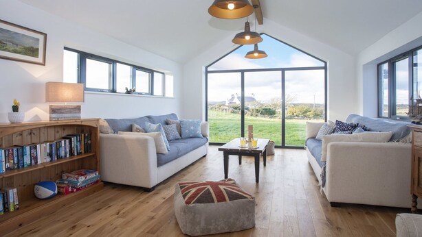 A spacious living room with a high ceiling, large windows, and a wooden floor. - Mwythus (Holyhead)