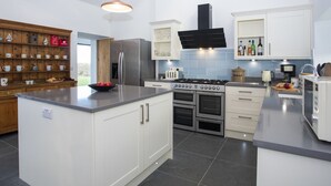 A modern kitchen with white cabinets, a stainless steel refrigerator, a gas stove, and a built-in oven. - Mwythus (Holyhead)