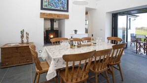 A dining area with a round table, six wooden chairs, a fireplace, and a large abstract painting on the wall. - Mwythus (Holyhead)