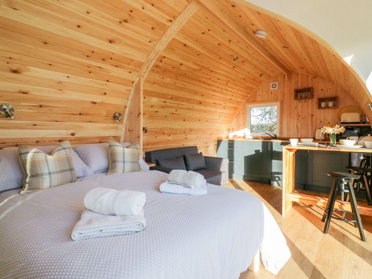 A cozy wooden cabin with a large bed, a sofa, and a kitchen area.