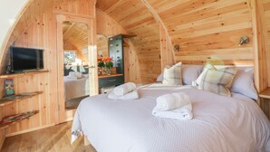 A cozy, wooden cabin bedroom with a bed, a TV, and a vanity with a mirror. - Chapel Pod (Saltash)