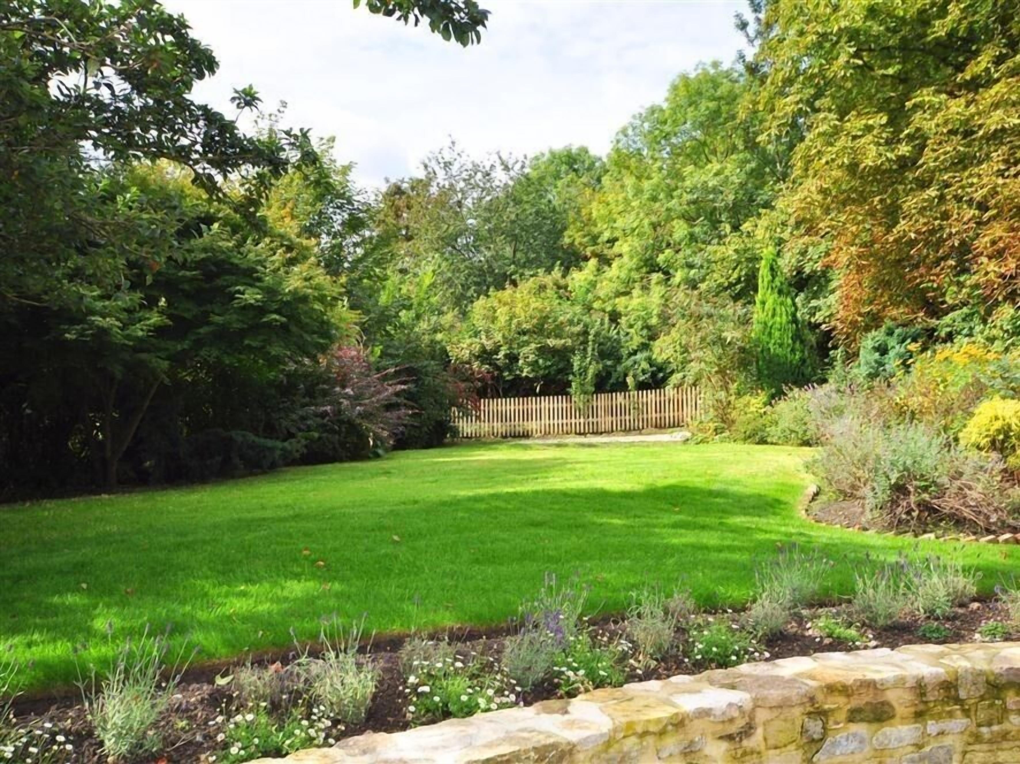 Ein gepflegter Garten mit Rasen, Steinrand und Holzlattenzaun.