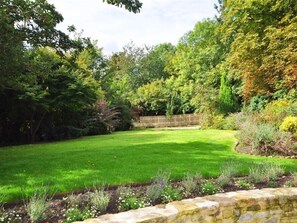 A well-maintained garden with a lawn, stone wall, and various plants.
