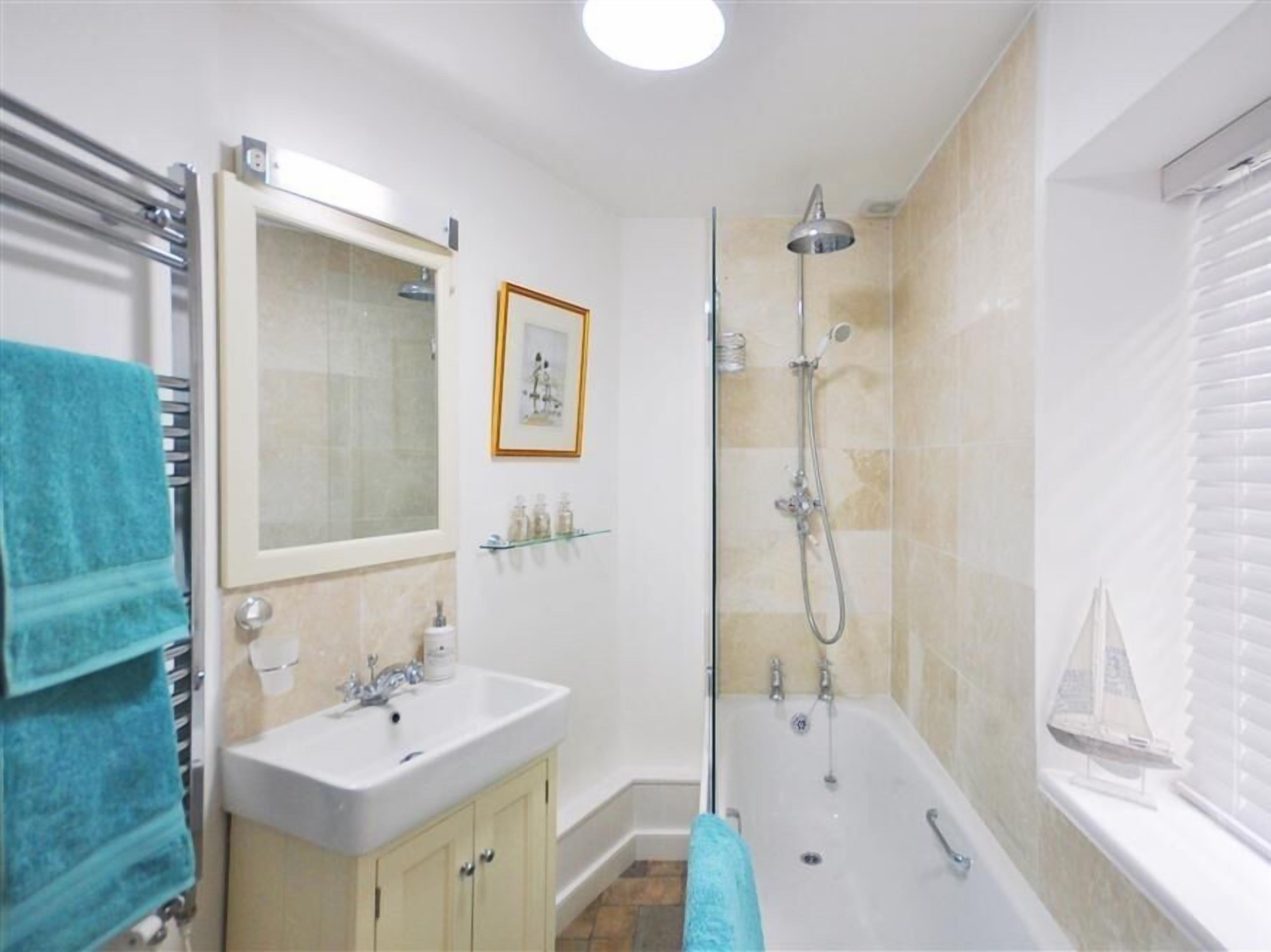 A bathroom with a bathtub, a shower, a sink, a mirror, and a framed picture on the wall.