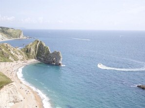 A coastal beach with a prominent rock formation, clear blue waters, and a sandy shoreline. - Warmwell Lodge (Dorchester)