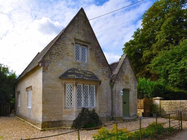 A stone building with a triangular roof, a small porch, and a green door.