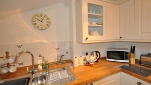 A kitchen with a sink, a microwave, a clock, and cabinets. - Warmwell Lodge (Dorchester)