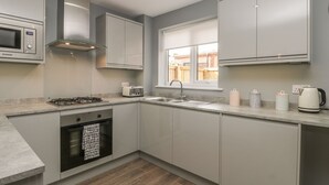 Una cocina moderna con gabinetes grises, horno empotrado, cocina a gas, campana extractora de acero inoxidable, ventana y pileta.