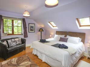 A bedroom with a large bed, a window with curtains, a sofa, and a skylight. - Tyddyn Morthwyl (Criccieth)