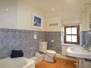 A bathroom with a bathtub, toilet, and sink, featuring tiled walls and a wooden floor. - Tyddyn Morthwyl (Criccieth)