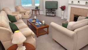 A living room with a sofa set, a coffee table, a lamp, a television, a fireplace, and a bookshelf. - Weymouth Bay Apartment B (Weymouth)