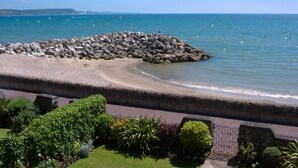 A coastal view with a rocky breakwater, a paved walkway, and lush greenery. - Weymouth Bay Apartment B (Weymouth)