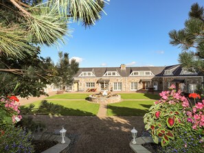A stone building with a well-maintained lawn, a fountain, and a variety of flowers. - Tyn Towyn - Ty Piws (Holyhead)