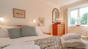 Una camera da letto ordinata con un letto, cuscini, una cassettiera e uno specchio.