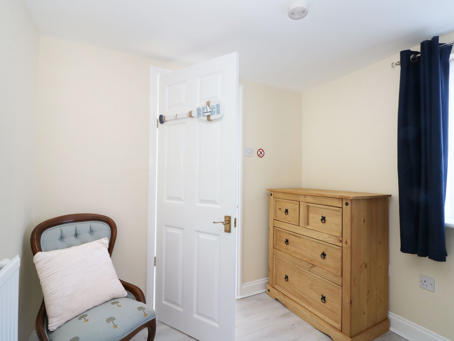 A room with a white door, a wooden dresser, a chair with a cushion, and a radiator.