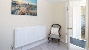 Una habitación con un radiador blanco, una silla de madera con cojín y una puerta que da a otra estancia.