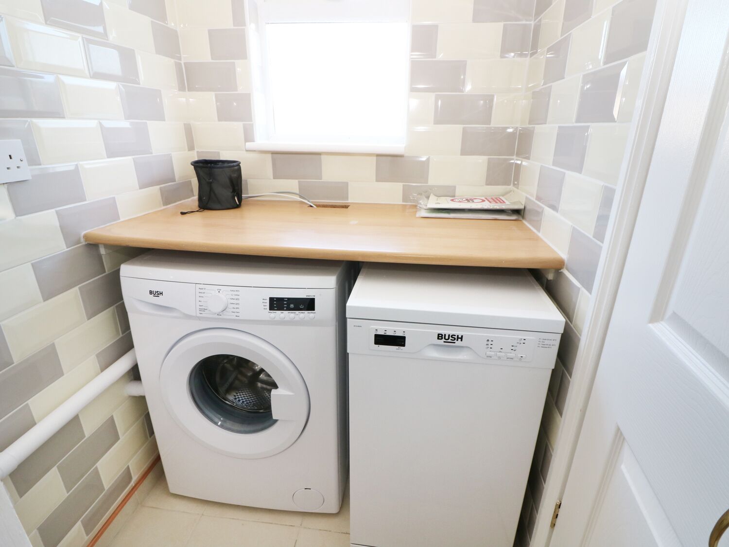 A compact laundry area with a washing machine and dryer, a wooden countertop, and tiled walls.