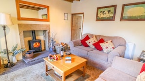 A cozy living room with a fireplace, a sofa, a coffee table, and a rug. - Rose Cottage (Skipton)